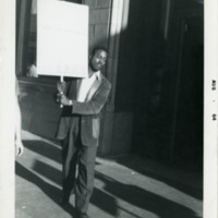 Man holding a sign and marching on the sidewalk, 1964